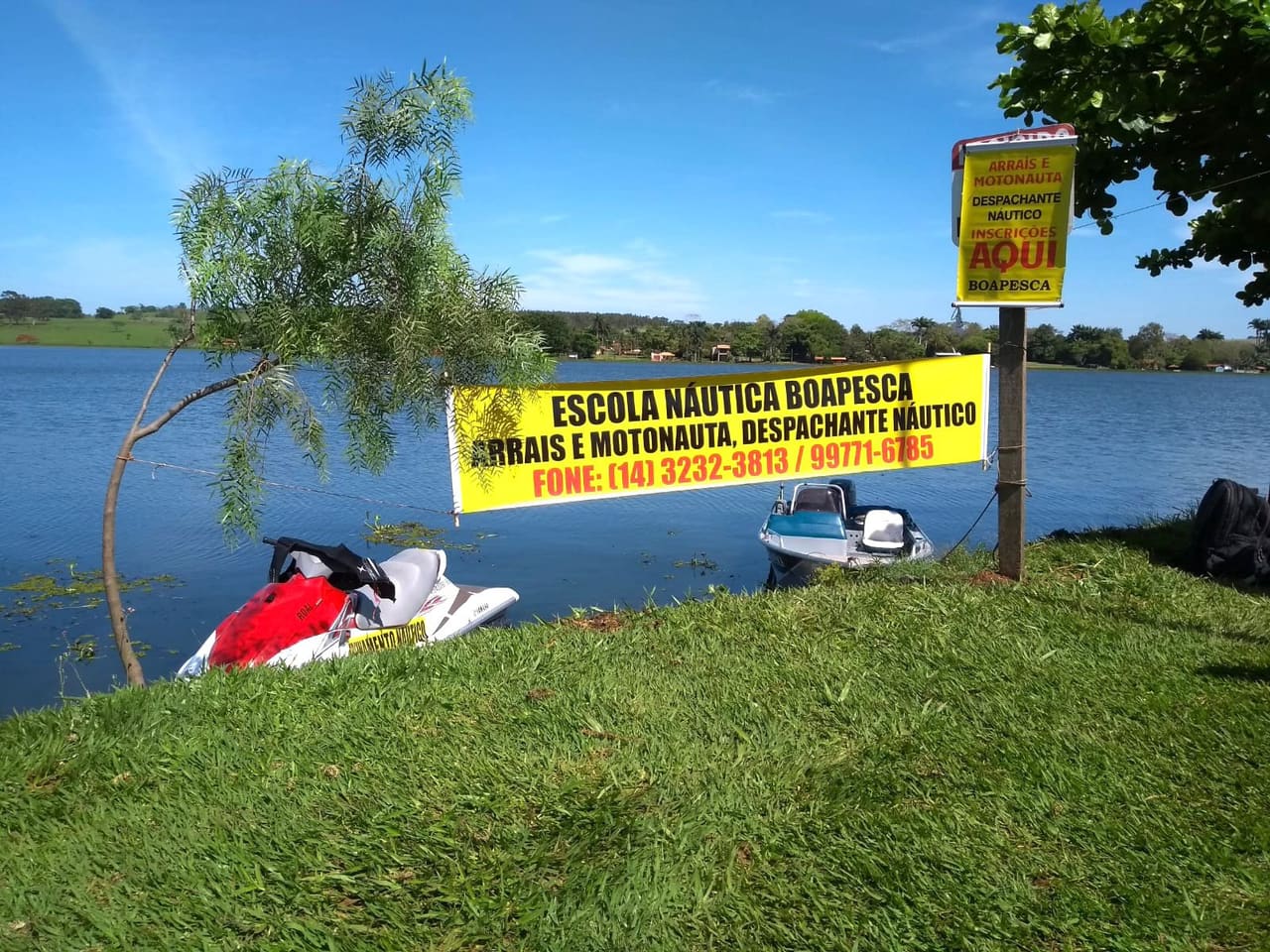 Banner da Escola Náutica BoaPesca na beira da represa, com a lancha e a moto aquática atracadas