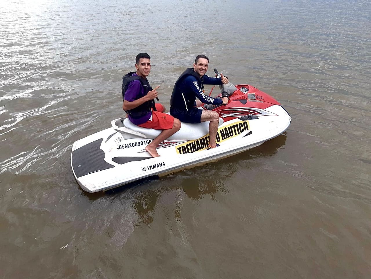 Instrutor conduzindo a moto aquática com o aluno na garupa