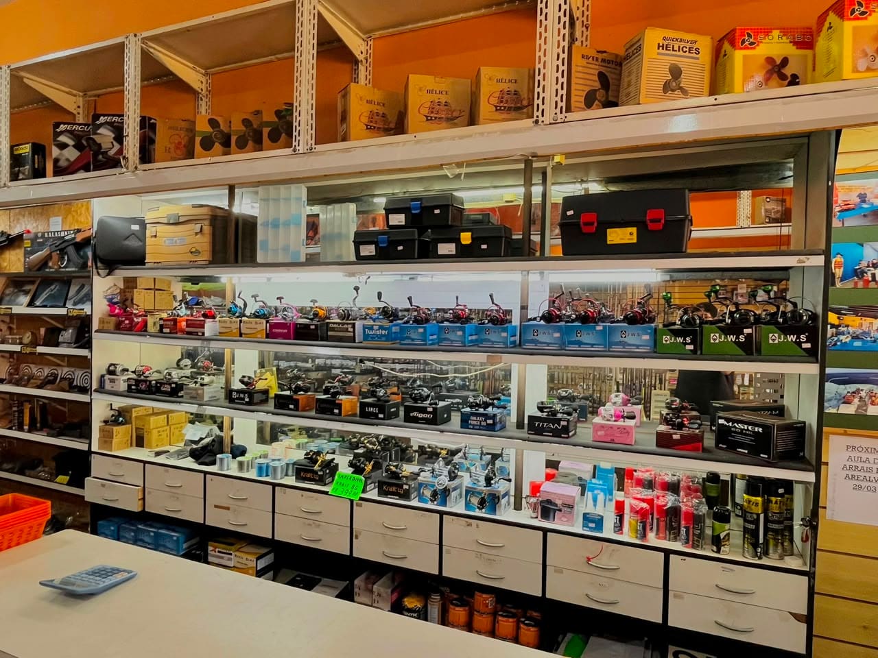 Vitrine de molinetes e carretilhas, com hélices de motor de popa na prateleira de cima