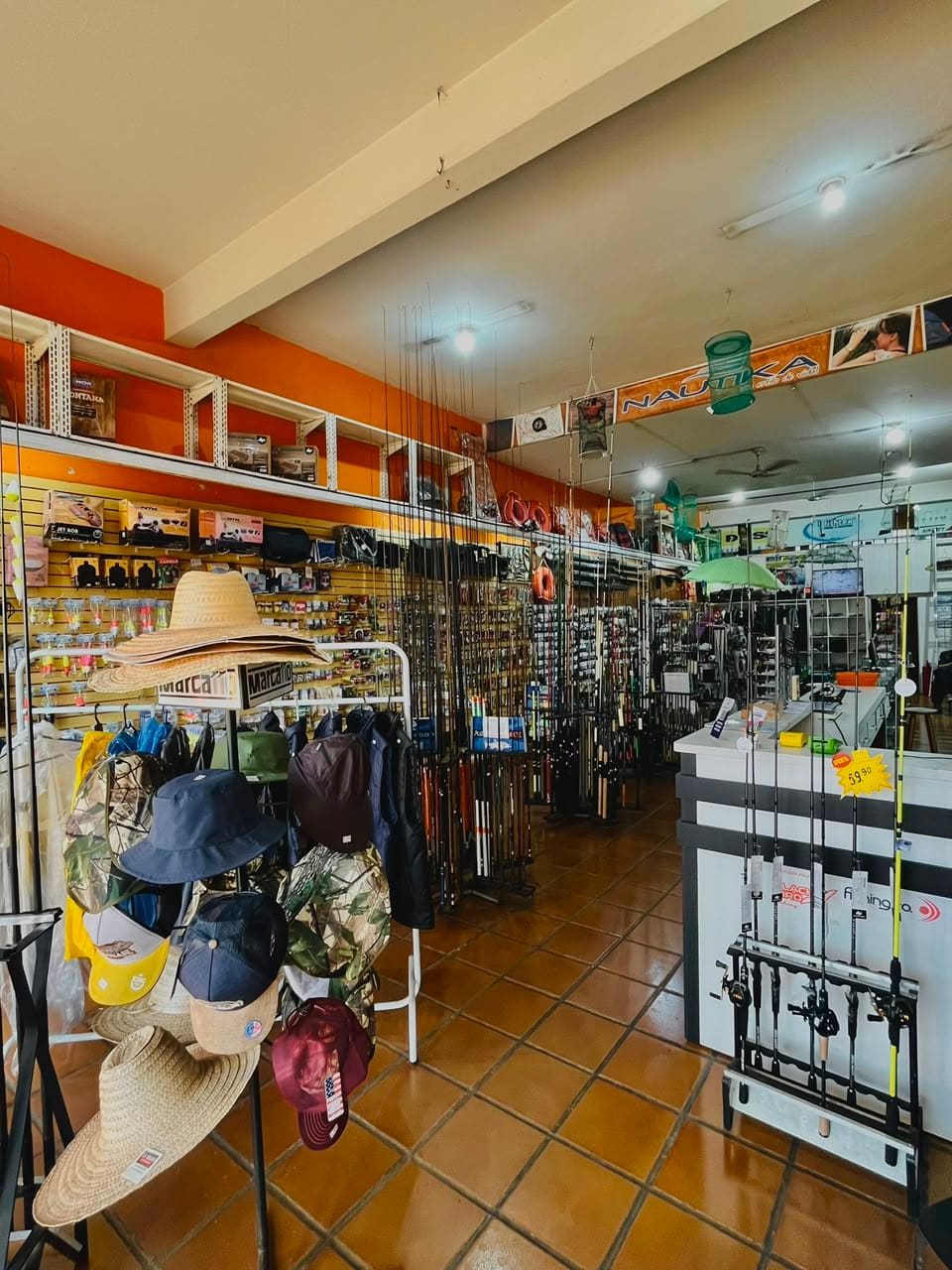 Arara de chapéus de palha, bonés e camisas de pesca na entrada da loja